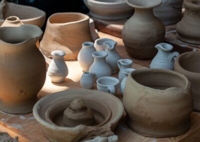 A collection of handmade clay pottery, showcasing diverse shapes and designs, displayed outdoors in natural light.